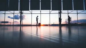 Silhouette of a man standing in a quiet airport terminal with glass window behind him.